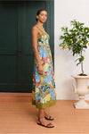 Woman wearing a colorful floral dress standing in a room with a plant and green door from Alemais