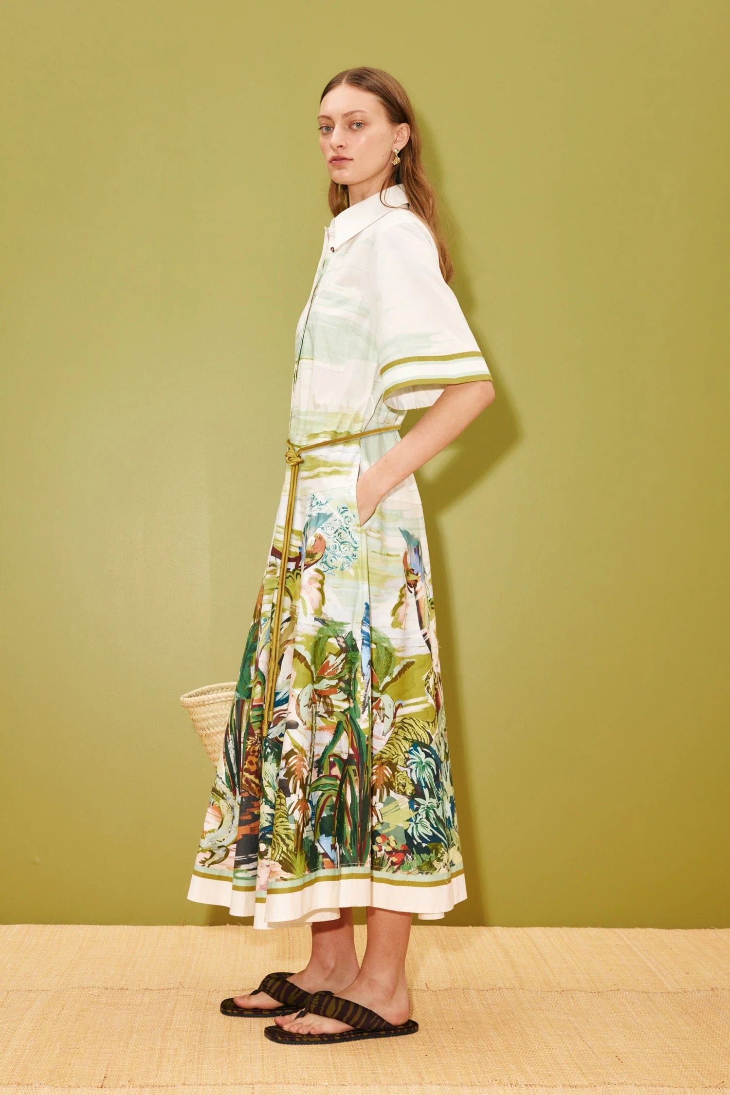 Side view of Woman wearing a white dress with a coluorful floral pattern against a green wall from Alemais