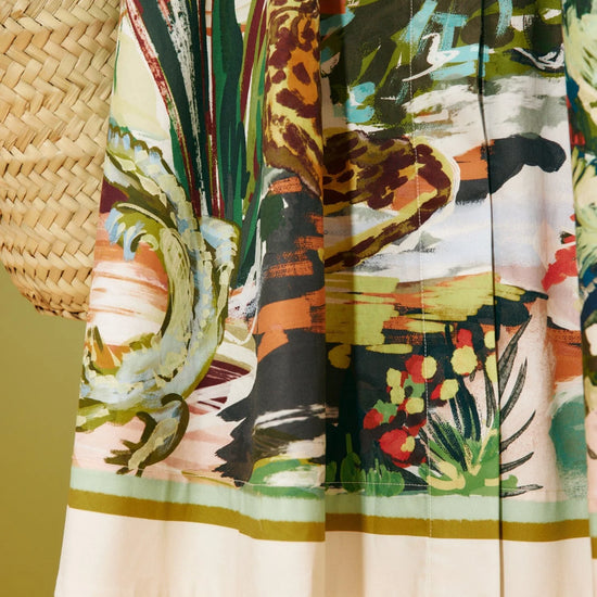 Colourful dress with a nature-themed print held by a person against a green background from Alemais
