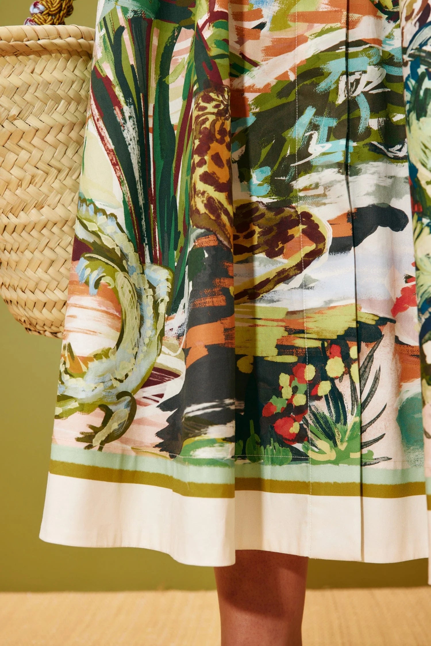 Colourful dress with a nature-themed print held by a person against a green background from Alemais