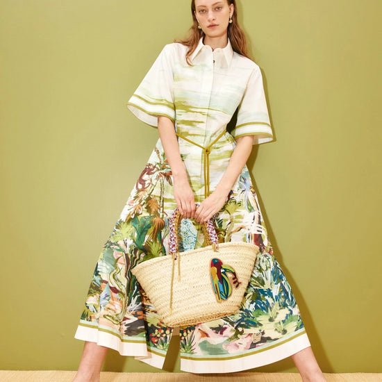 Woman in a floral dress holding a woven bag against a green background
