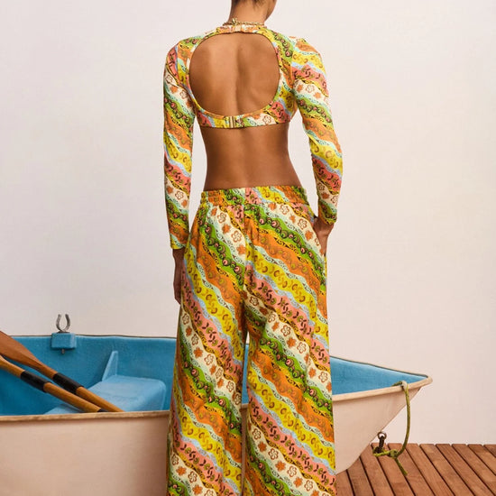 Woman in a colorful patterned outfit standing by a small boat on a wooden deck.