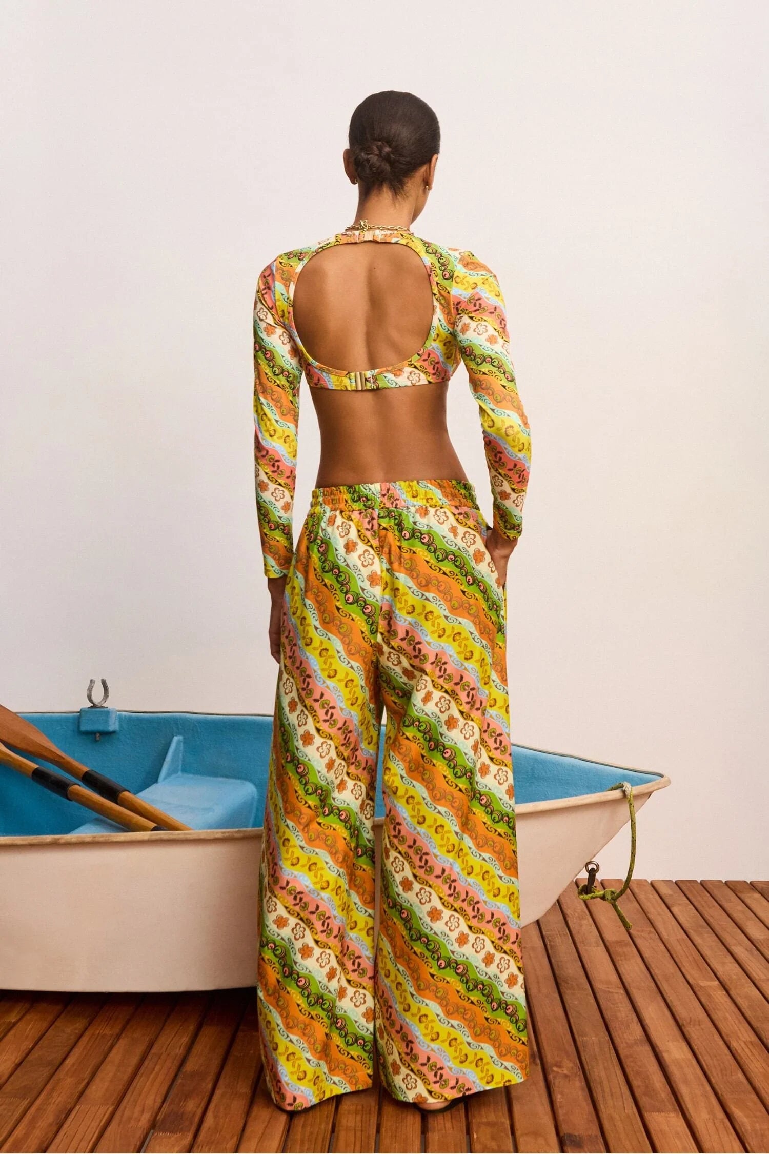 Woman in a colorful patterned outfit standing by a small boat on a wooden deck.