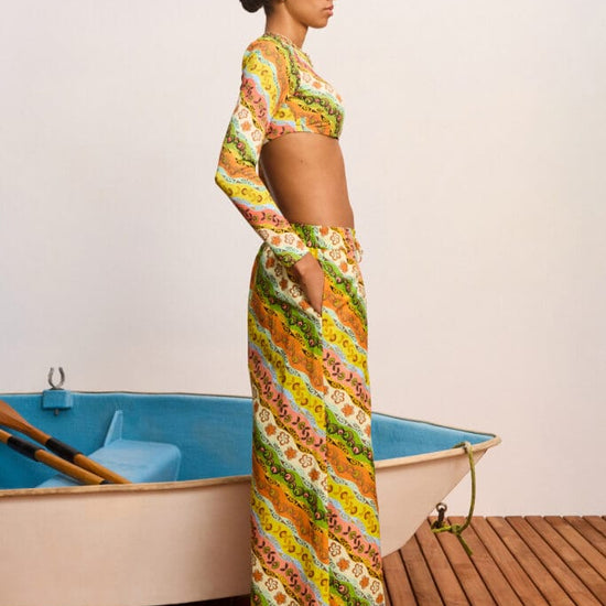 Woman in a colorful patterned outfit standing next to a small boat on a wooden deck.