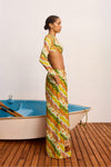 Woman in a colorful patterned outfit standing next to a small boat on a wooden deck.