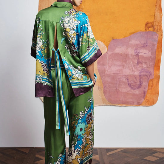 Woman wearing a colorful outfit with a patterned shirt and pants by Alemais against an abstract wall rear view