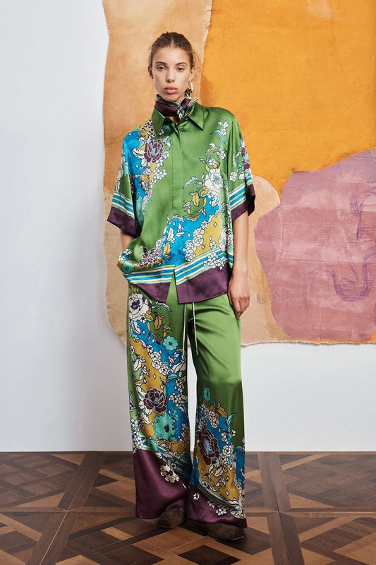 Woman wearing a colorful outfit with a patterned shirt and pants by Alemais against an abstract wall.