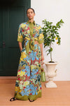 Woman wearing a colorful floral outfit standing in a room with a plant and door.