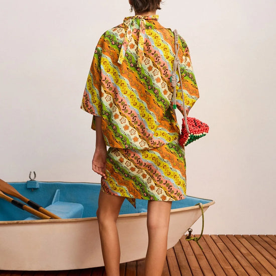 Woman in a colorful patterned dress standing next to a small boat on a wooden deck.