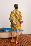 Woman in a colorful patterned dress standing next to a small boat on a wooden deck.
