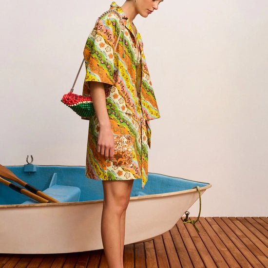 Woman in a colorful dress standing next to a small boat on a wooden deck.