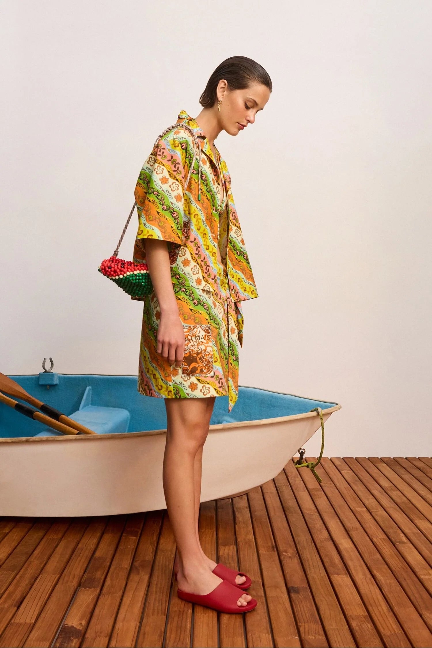 Woman in a colorful dress standing next to a small boat on a wooden deck.