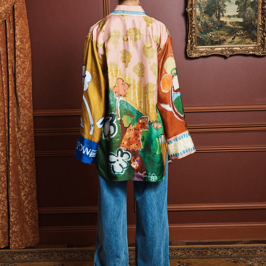 Person wearing a colorful shirt by Alemais and blue jeans in an elegant room with a painting on the wall rear view