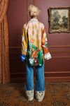 Person wearing a colorful shirt by Alemais and blue jeans in an elegant room with a painting on the wall rear view
