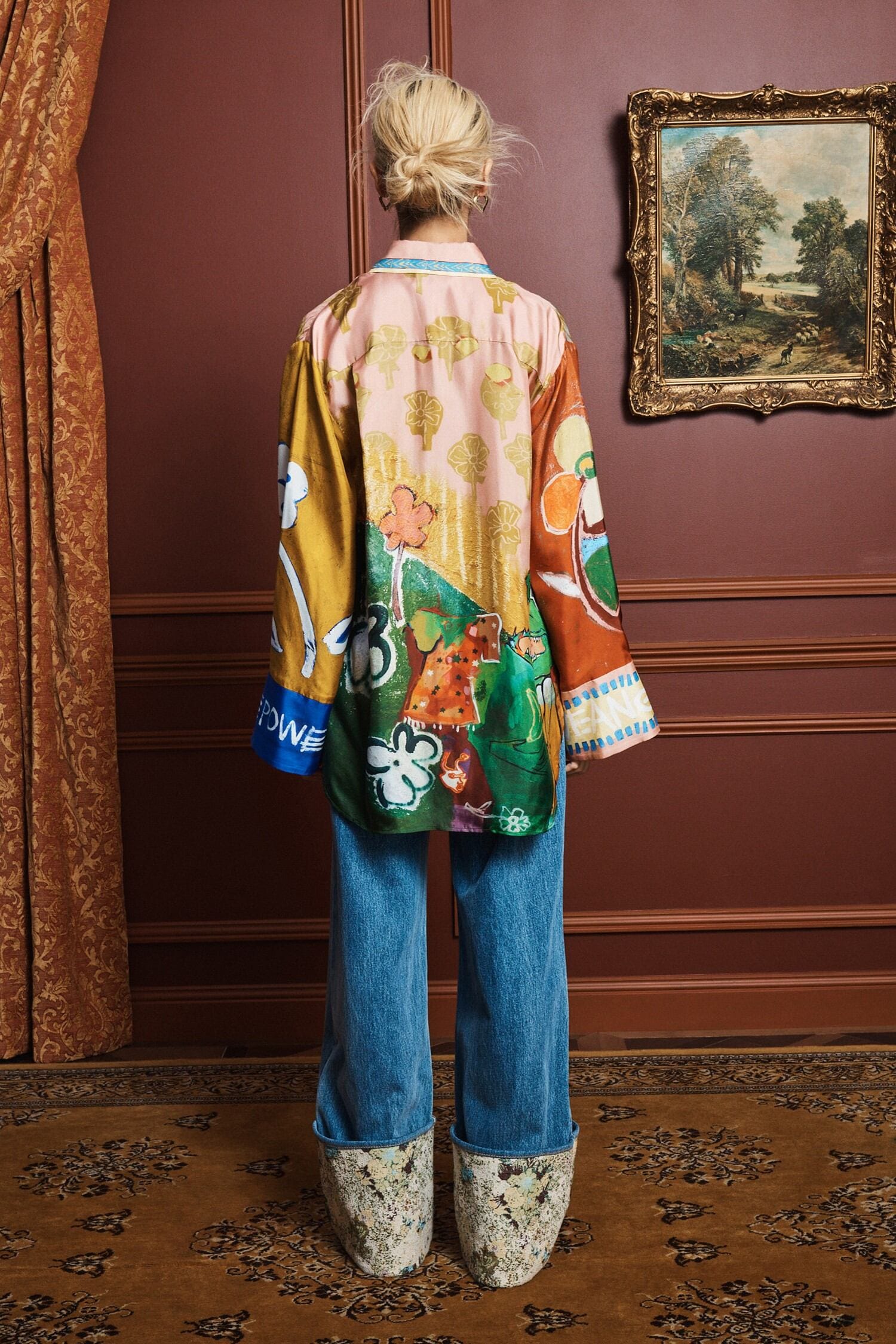 Person wearing a colorful shirt by Alemais and blue jeans in an elegant room with a painting on the wall rear view