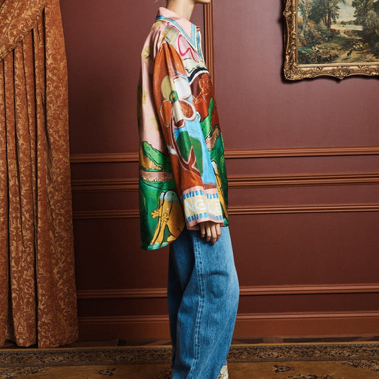 Person wearing a colorful shirt by Alemais and blue jeans in an elegant room with a painting on the wall side view