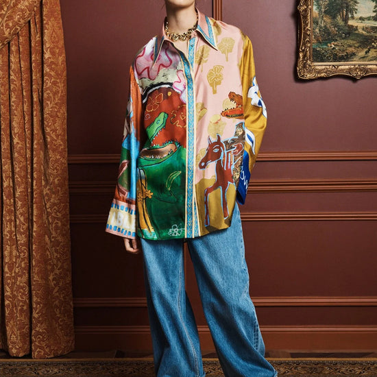 Person wearing a colorful shirt by Alemais and blue jeans in an elegant room with a painting on the wall.