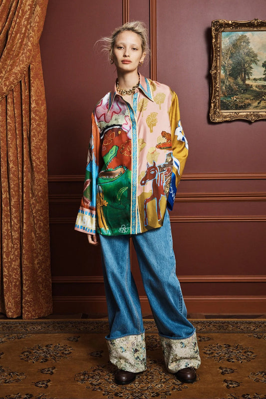 Person wearing a colorful shirt by Alemais and blue jeans in an elegant room with a painting on the wall.