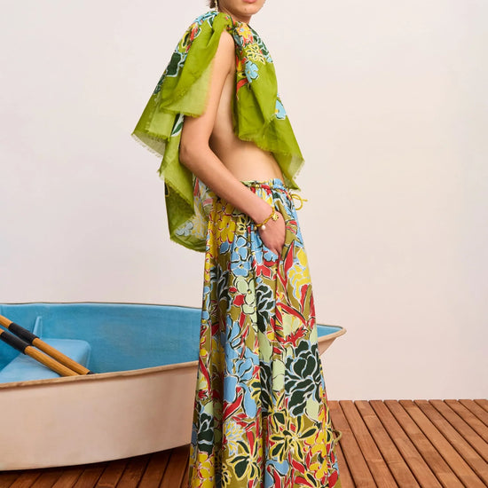 Woman in colorful floral dress standing on a wooden deck with a small boat in the background.