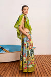 Woman in colorful floral dress standing on a wooden deck with a small boat in the background.
