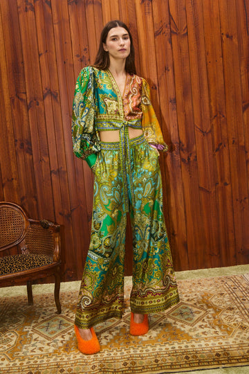 Woman wearing a colorful patterned outfit in a room with wooden walls and a textured rug.