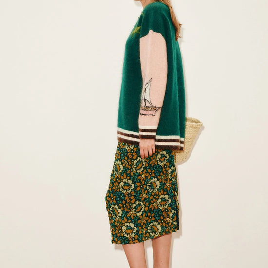 Woman wearing a green cardigan and patterned skirt on a white background from Alemais