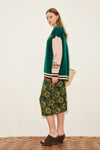Woman wearing a green cardigan and patterned skirt on a white background from Alemais