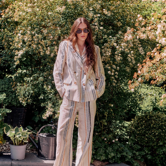 Woman in a striped suit standing outdoors with greenery in the background