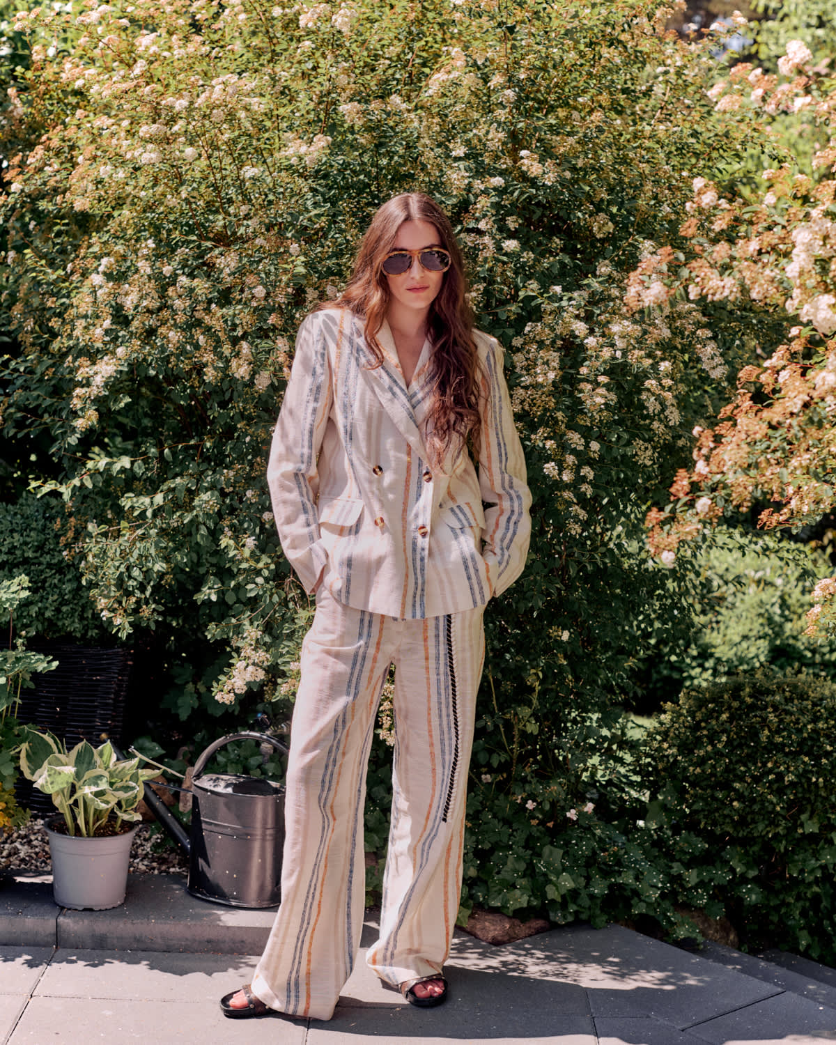 Woman in a striped suit standing outdoors with greenery in the background