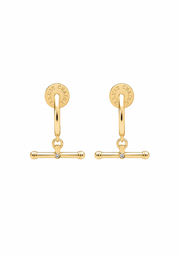 A pair of gold huggie hoop earrings with a dangling barbell charm and a small clear rhinestone in the center, shown on a plain white background.