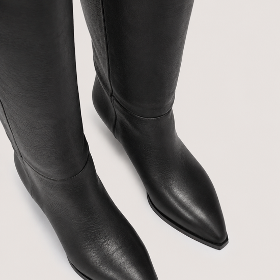 Black leather pointed-toe knee-high boots shown from a high-angle close-up on a light gray background.