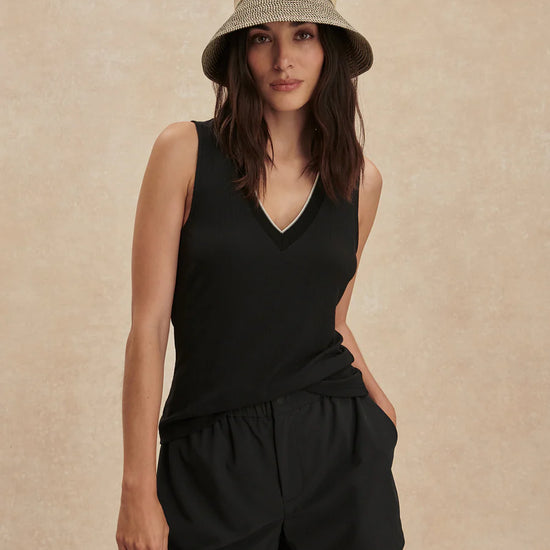 Woman wearing a black sleeveless top and shorts with a beige hat on a beige background
