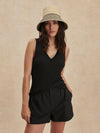 Woman wearing a black sleeveless top and shorts with a beige hat on a beige background