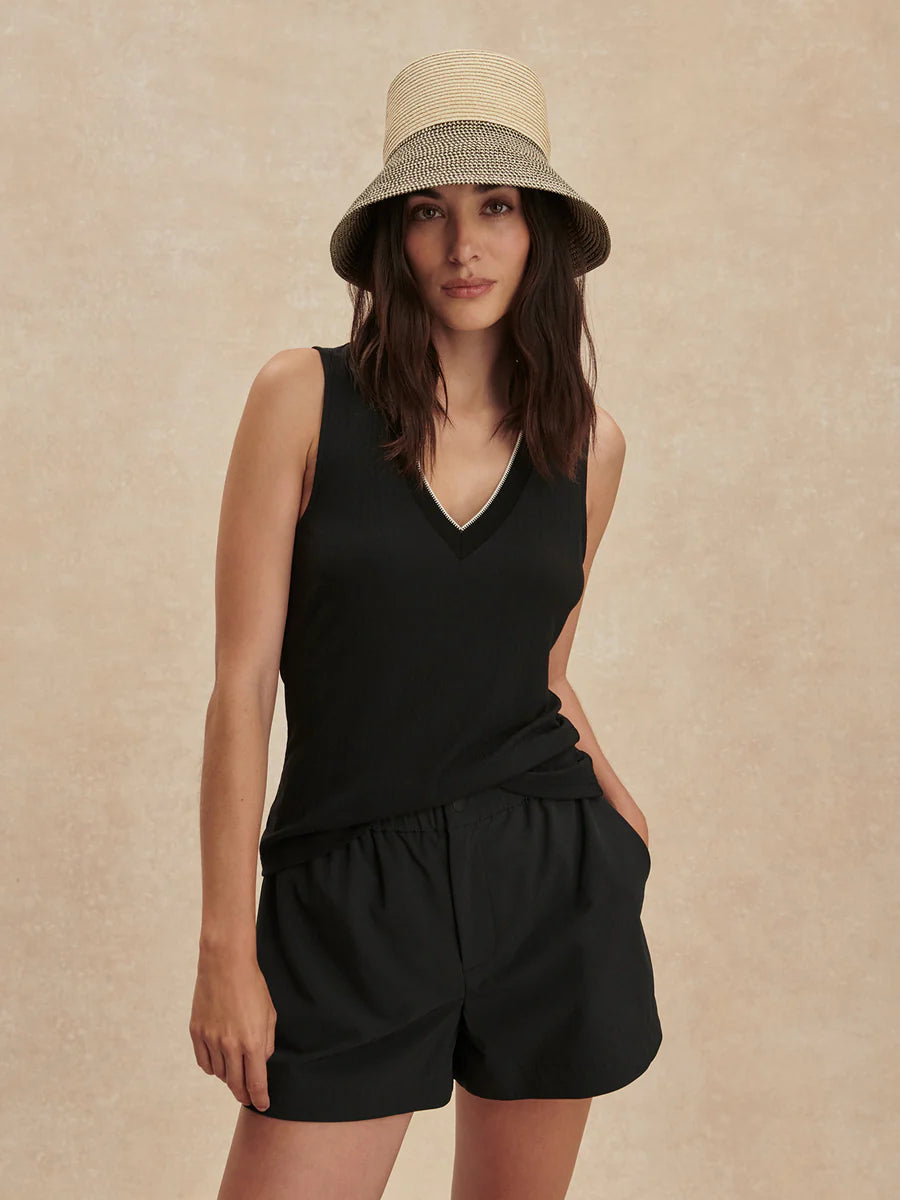 Woman wearing a black sleeveless top and shorts with a beige hat on a beige background