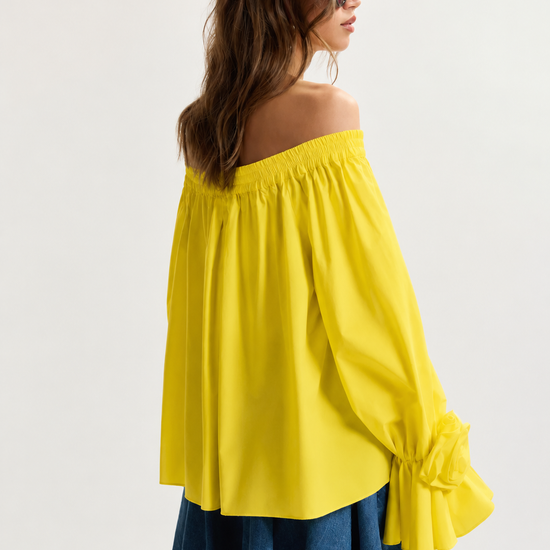 Woman wearing a yellow off-shoulder top and denim shorts on a white background
