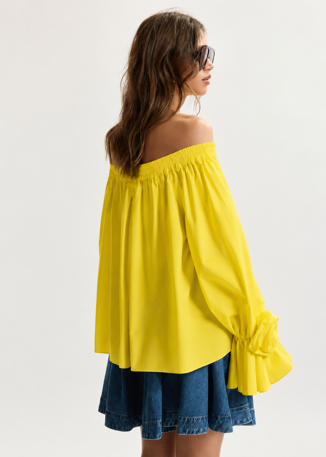 Woman wearing a yellow off-shoulder top and denim shorts on a white background