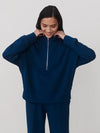 A woman wearing a navy blue half-zip sweatshirt and matching navy blue sweatpants, posing against a light gray studio background.