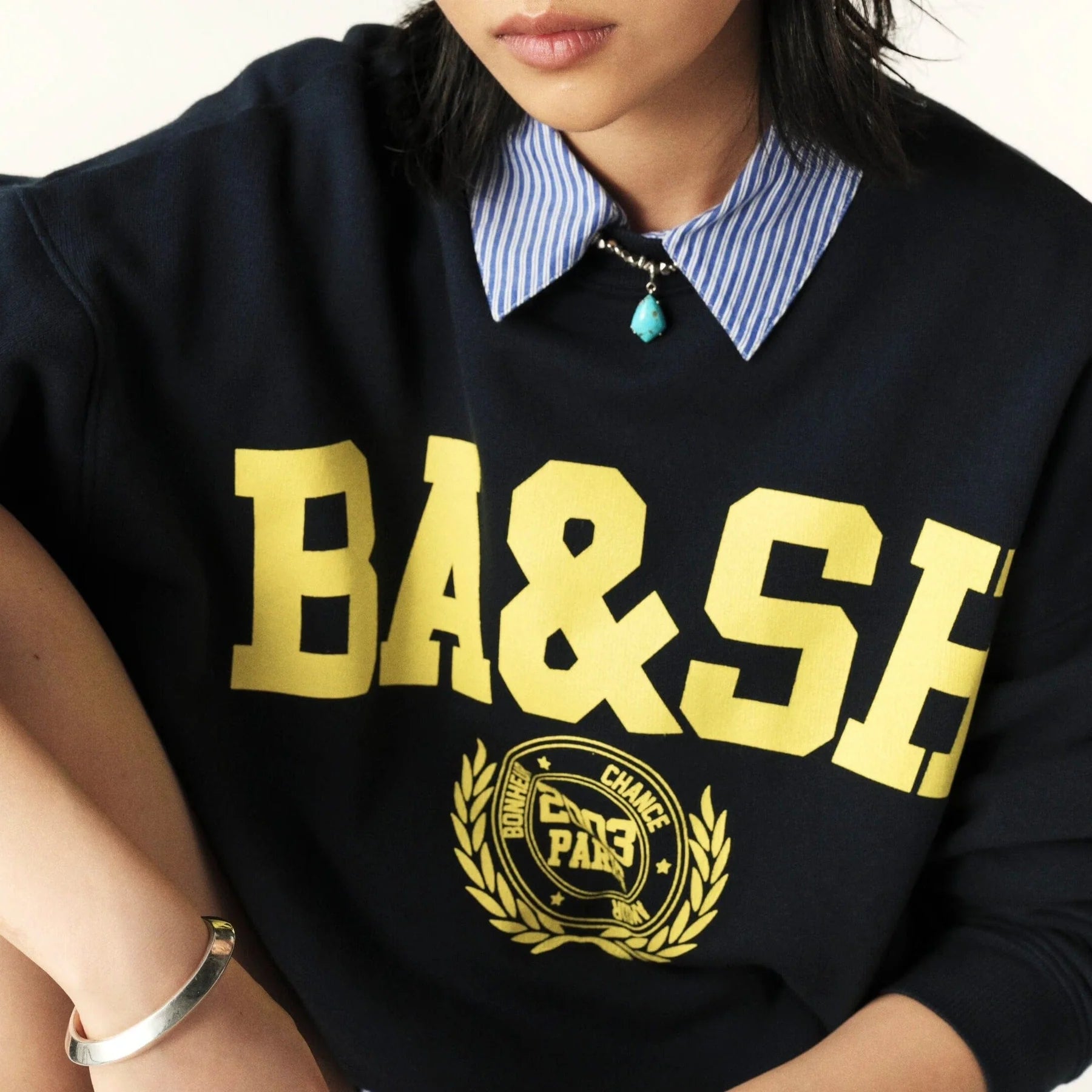 Navy sweatshirt with yellow ba&sh branding worn with striped shirt