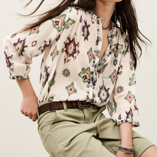 Woman wearing a floral blouse and beige shorts against a neutral background
