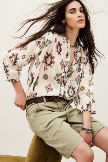 Woman wearing a floral blouse and beige shorts against a neutral background