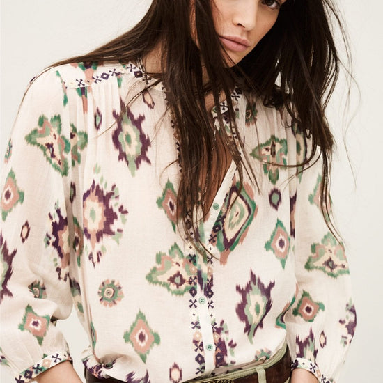 Woman wearing a patterned blouse with a belt and beige pants on a white background from ba&sh