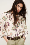 Woman wearing a patterned blouse with a belt and beige pants on a white background from ba&sh