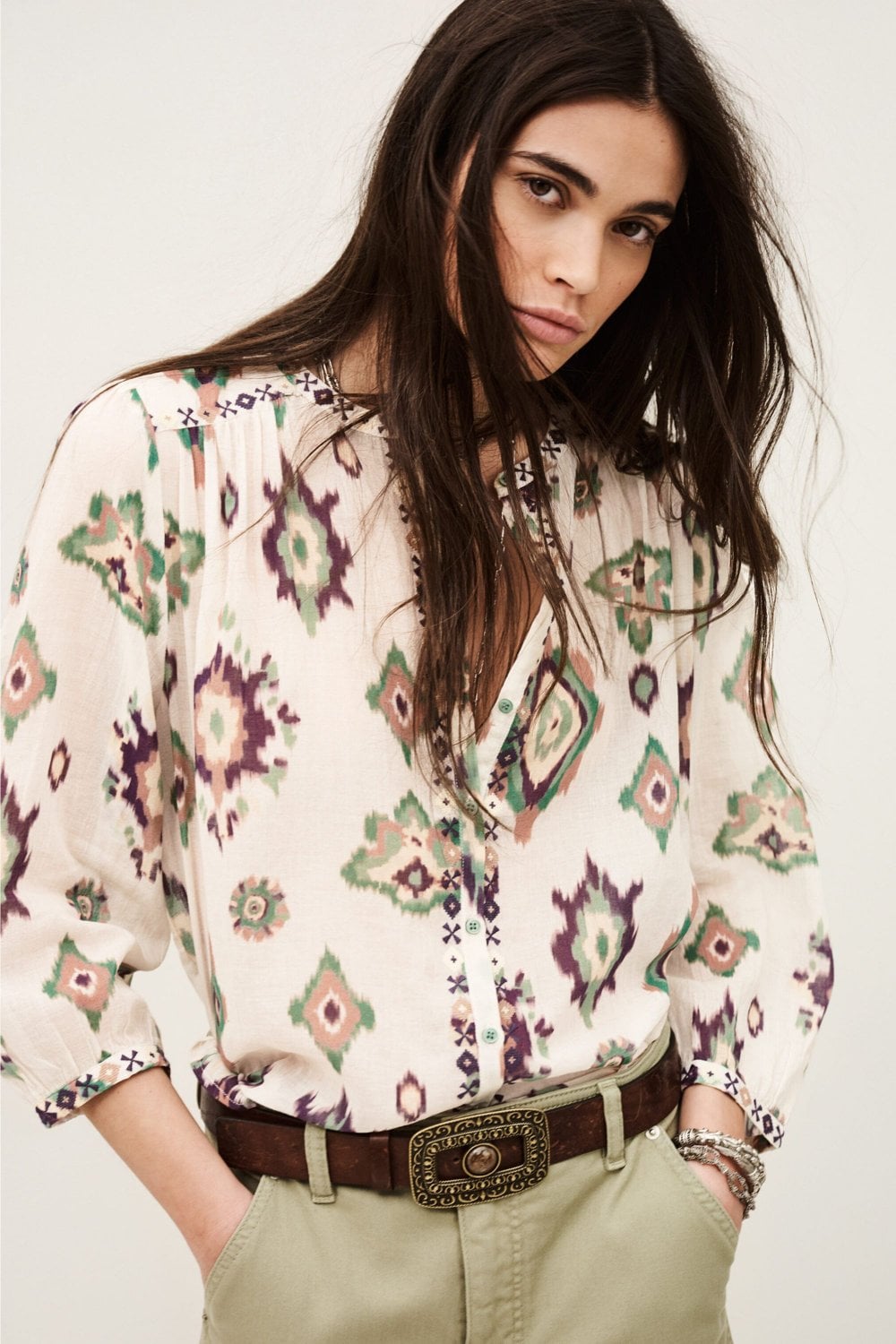 Woman wearing a patterned blouse with a belt and beige pants on a white background from ba&sh