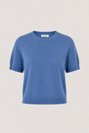 A short-sleeve crewneck knit sweater in a medium blue color, displayed on a neutral light beige background.