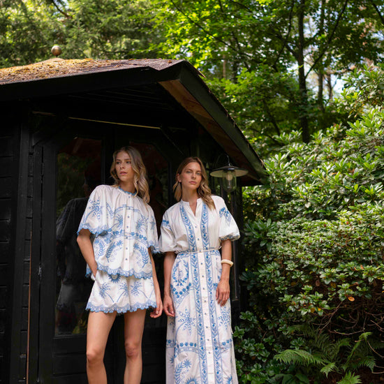 Two women in matching patterned outfits standing in a garden setting.