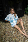 Woman in a blue and white patterned outfit sitting on a gravel path.