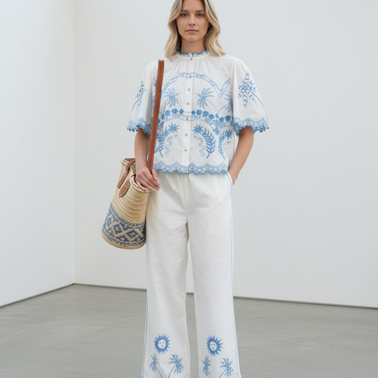 Woman wearing a white outfit with blue embroidery in a minimalistic setting