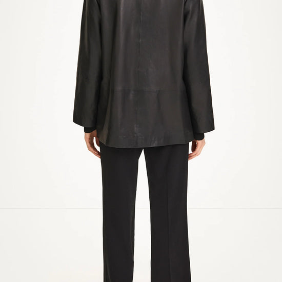 A model shown from the back wearing a black leather jacket with a high mock neck, black wide-leg trousers, and black high-heeled sandals against a plain white studio background.