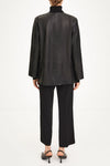 A model shown from the back wearing a black leather jacket with a high mock neck, black wide-leg trousers, and black high-heeled sandals against a plain white studio background.