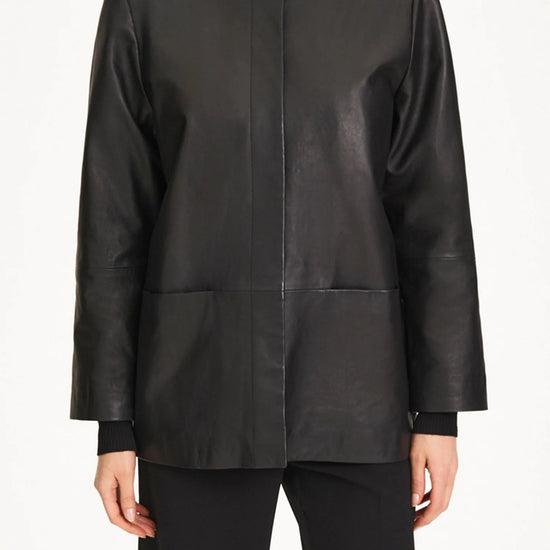 A model wearing a black leather jacket with a high mock neck, long sleeves, and front patch pockets, paired with black trousers.